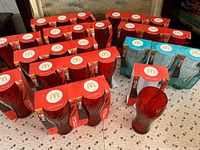 Photo showing multiple boxed and unboxed McDonald's limited edition Coca Cola glasses in red and blue colors arranged on a table.