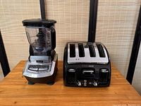 Side-by-side view of Ninja professional blender and Tfal 4-slice toaster on wooden surface with bamboo backdrop