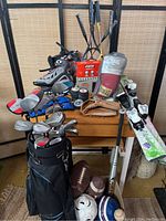 Photo showing entire sports lot on table including golf clubs, inline skates, tennis rackets, boxing gloves, hockey pucks, balls, weights, and bat