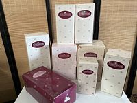 Photo showing eight boxed dolls from Ashton-Drake Galleries in various original packaging, grouped together on a beige backdrop.