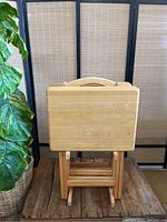 Front view of four wooden TV tables standing upright showing the flat table tops and handles.