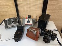 Full lot of five vintage cameras and one flash unit together on white surface