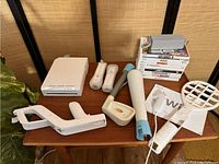 Photo showing Nintendo Wii console, 2 Wii remotes with sleeves, 5 gaming accessories, 9 Wii game cases, and manual.
