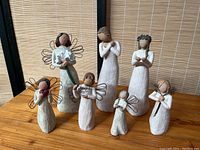 Full set of seven Willow Tree figures displayed on wooden surface against bamboo backdrop