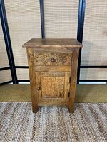 Front view of small wooden farmhouse style side table showing decorative carved drawer and cabinet door with round wooden knobs.
