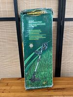 Front view of the green Yardworks cardboard box with image and branding of the cordless grass trimmer/edger and product features.