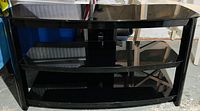 Black lacquer TV console with three tiers consisting of a top surface and two glass shelves supported by black lacquer frame.