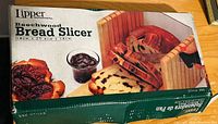 Photo of the boxed Lipper Beechwood Bread Slicer featuring the bread slicer with wooden guide and serrated knife, with bread and jam for scale.