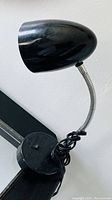 Photo showing a black desk lamp with flexible gooseneck and oval-shaped lampshade, circular base, and cord wrapped around the base.