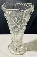Photo of a clear glass vase with etched flower patterns, scalloped rim, and faceted base on a white surface with black background