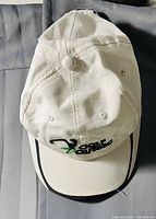 Top angle photo of a white golf hat showing embroidered logo and black trim on curved bill.