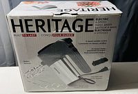 Photo of Heritage 6-speed electric hand mixer in box showing beaters, accessory holder, and attachments.