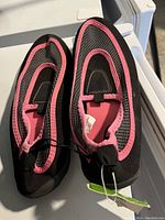Top angle photo of new girls swim shoes size 5/6 in black and pink, showing both shoes side by side with tags attached.