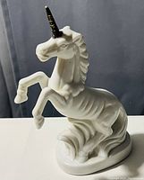 White porcelain unicorn figurine with gold-colored horn, rearing on hind legs with detailed design and smooth oval base.