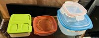 Photo of six plastic storage containers with lids including green, orange, and blue lids in various sizes, on a dark surface