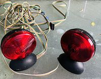 Two round red trailer lights with wiring harness on a glass surface. The lights have black bases and multiple colored wires attached for connectivity.