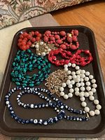 Top view of a tray holding seven assorted beaded necklaces in red, coral, turquoise, white, and blue colors.