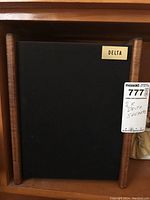 Front view of Delta speaker showing wood casing and black fabric with a brass brand plate 'DELTA'