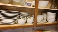Open shelf view showing stacks of dinner plates, salad plates on left, bowls on right with sugar bowl and creamer in front