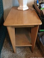 Front view of one wooden end table with flat top surface, tapered sides, and open shelf below.