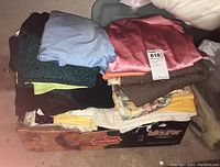 Assorted fabric remnants stacked on top of a box, showing various colors and patterns including pink, blue, black with dots, and floral prints.