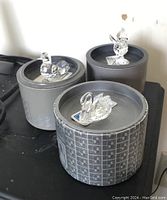 Three Swarovski crystal figurines displayed on their boxes: swan and two birds, each clear crystal, approximately 1-2 inches tall with intricate detailing, placed on round boxes with Swarovski logos.