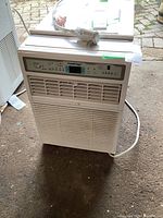 Full view of the white KoolKing window air conditioner unit showing vents, power cord, and remote on top.