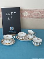 Photo showing the full set including cup, saucer, sugar bowl with lid, creamer, and tray with a black board indicating lot number
