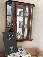 Curio cabinet with glass front door and curved glass sides mounted on wall. Inside visible are multiple angel figurines on three glass shelves, mirrored back inside cabinet.