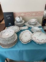 Full set layout showing various stacked dinner plates, serving platters, soup bowls, cups and saucers, and covered tureen all displaying pink rose floral patterns with gold trim.