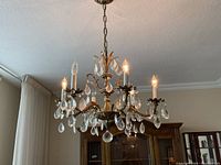 Crystal chandelier hanging from ceiling with lit candle bulbs and clear crystal teardrop droplets hanging from metal arms and base.