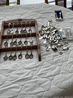 Wide view showing wooden spoon rack with 20 spoons arranged and additional spoons scattered on cloth surface