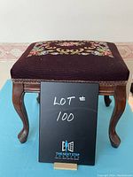 Front view of vintage burgundy stool showing embroidered floral cushion and curved wooden legs.