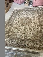 Full view of the floral area rug showing overall pattern and size on a beige carpeted floor with nearby pink upholstered chairs.