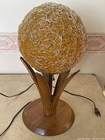 Front view of the vintage globe-shaped textured amber and clear glass lamp shade atop wood base with leaf-like supports and pull chain.