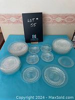 Full assortment of vintage glass dishes including multiple sizes of bowls, plates, and serving dishes laid out on a turquoise cloth.