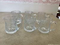Six clear glass mugs arranged in two rows showing the front side with floral embossed texture and handle.