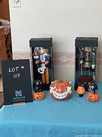 Photo showing the whole lot on a table with a lot number sign, displaying two boxed Halloween nutcracker figures, two black cat figurines on pumpkins, a pumpkin candy dish, and a small pumpkin tealight holder.