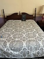 Full view of mahogany headboard with attached rails, bed made up with patterned bedding, flanked by nightstand and lamp