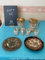 Photo of two carnival glass juice pitchers with matching four juice glasses, one spiral-patterned serving plate and one floral-patterned serving plate on table.