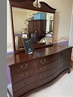 Front view of the dark mahogany dresser showing curved front and nine drawers with brass handles. Large mirror with decorative molding sits on top.