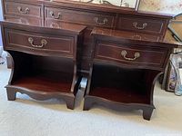 Pair of dark mahogany night tables shown side-by-side from the front, highlighting single drawer with decorative brass handle and open cubby below.