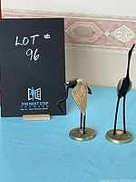Two metal crane sculptures on blue table, with one crane standing tall and the other with neck curved downward.