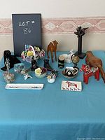 Overview photo showing assorted vintage nicknacks and figurines arranged on a blue tablecloth including animals, floral decor, and small sculptures.