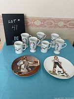 Seven white Norman Rockwell collector cups arranged behind two decorative plates on blue cloth, cups have colorful detailed character illustrations, plates with children and adult scenes.