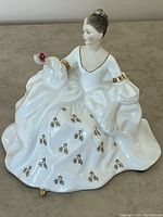 Front view of Royal Doulton porcelain figurine showing seated woman in white gown with gold accents and holding red rose.