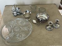 Wide shot showing all items in assortment: glass tray, glass bowls, silver plate creamer, bowl, spoon, candlesticks, condiment set.