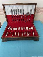 Full view of vintage silverplate cutlery set for six in original wooden case with red velvet interior and white fabric lid lining.