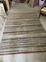 Photo showing the full view of the rectangular striped area rug placed on a beige carpeted floor, colors and pattern visible.