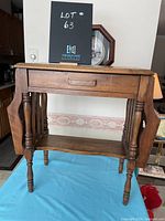 Front view of wooden telephone table showing drawer, turned legs, foldable side panels, and lower shelf on blue cloth background.